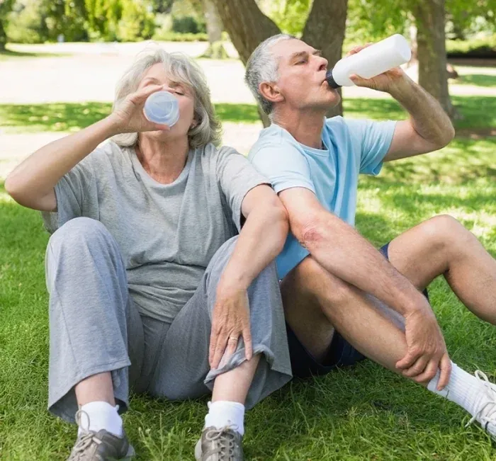 An older couple drinking water together on a park bench